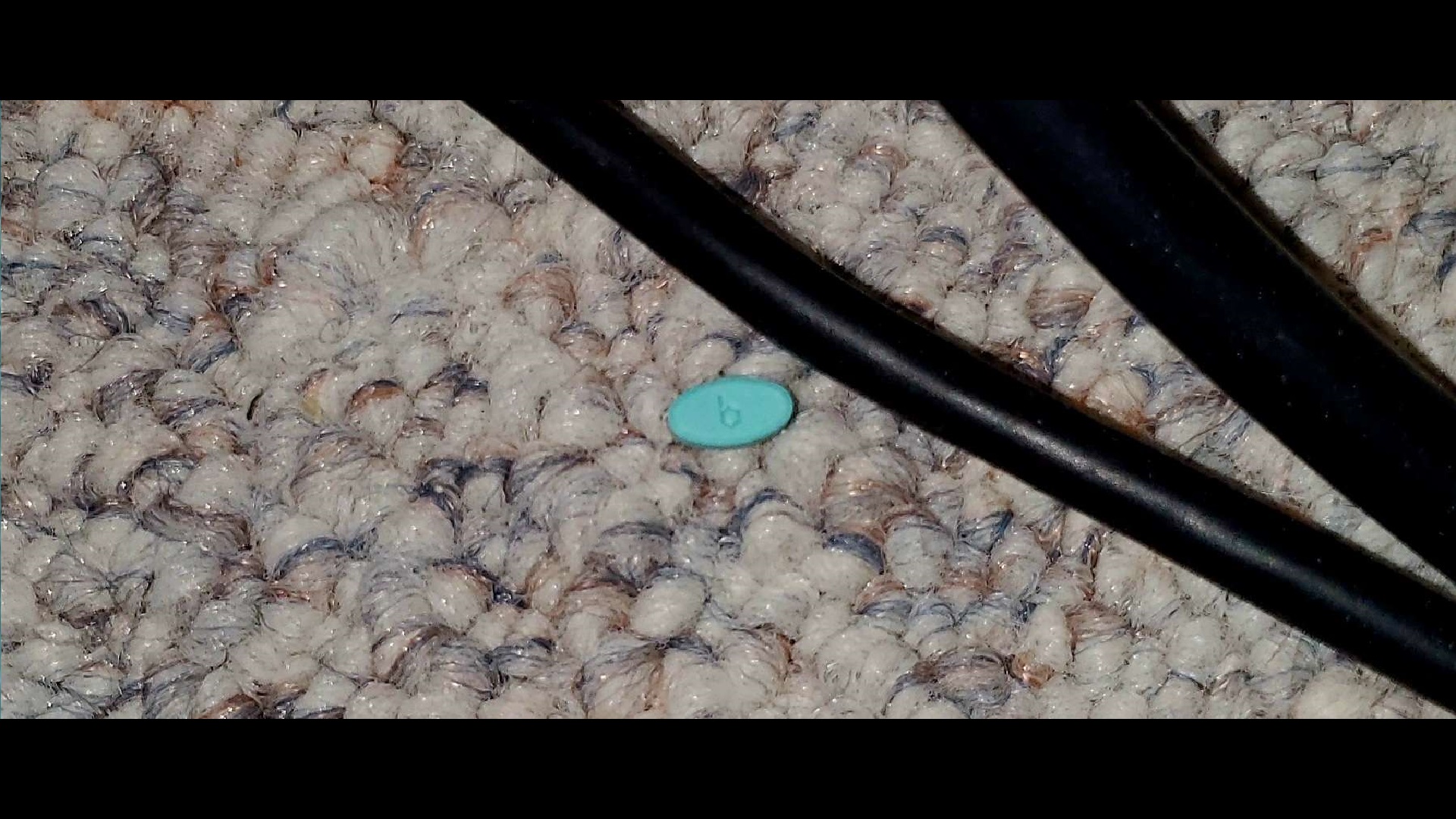 a small, oval shaped uncoated estrogen pill dropped on the carpet, below a few stray cords